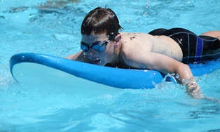 Male student paddling on a board in pool